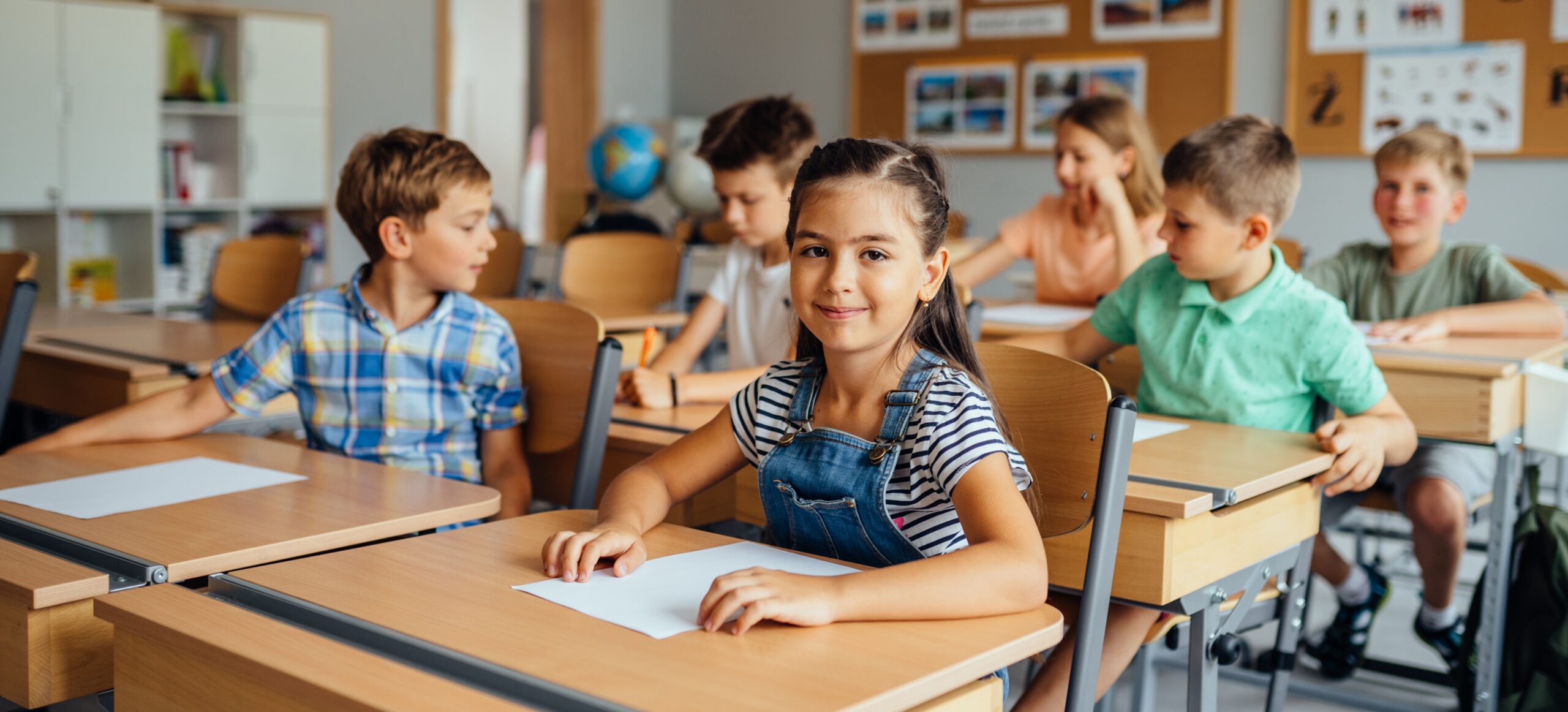 Children in the classroom at the lesson. Young cute hispanic girl looking at the camera. Classmates doing test tasks at school.