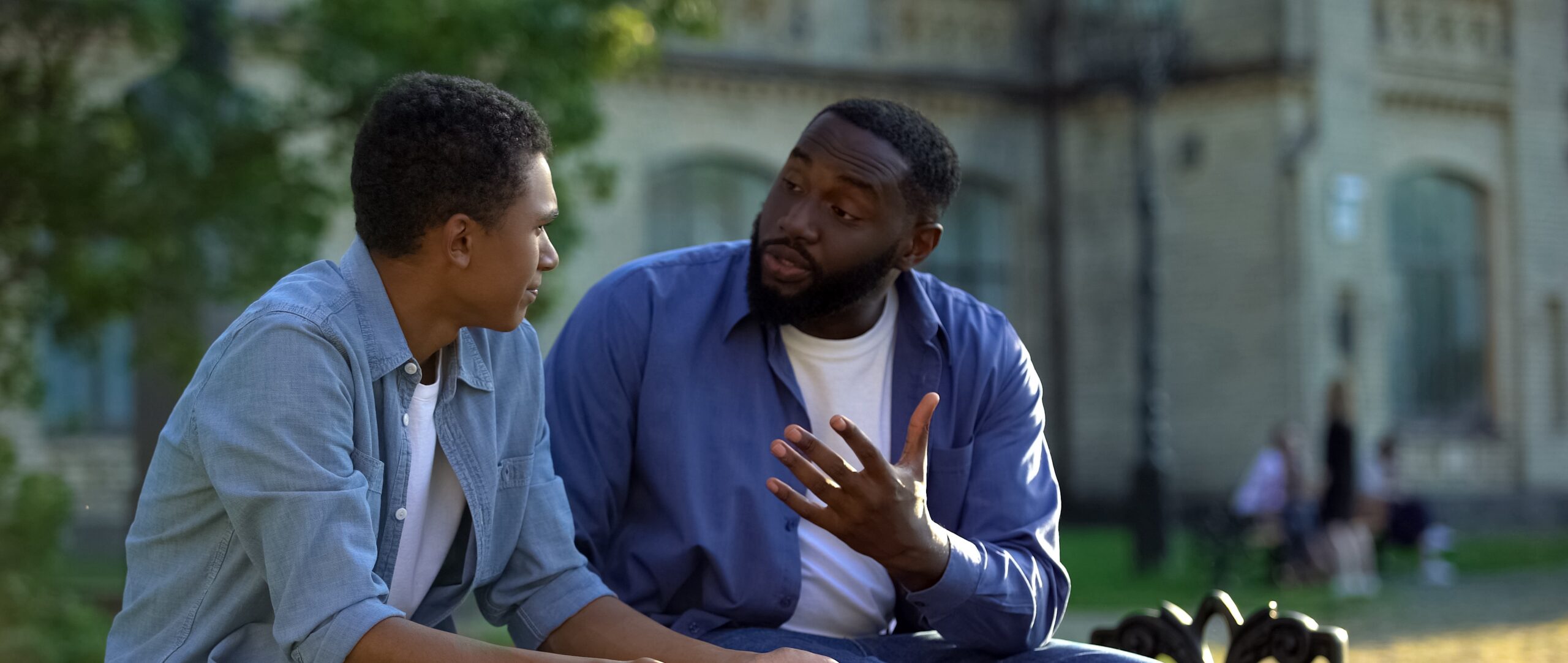 Father arguing teenage son sitting on campus bench, puberty age difficulties